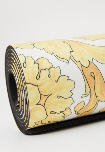 Jóga podložka s květinovým vzorem v žluté barvě na bílém pozadí, s texturovaným povrchem a černými okraji, stočená pro uskladnění.