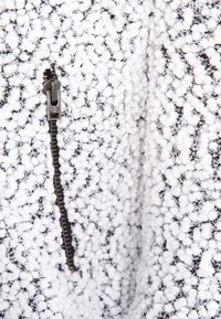 Ett svart- och vitt mönstrat tyg med en texturerad, fluffig yta. En synlig dragkedja löper längs mitten, med en liten dragflik.