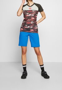 Košile krátkého rukávu s červeným a černým vzorem a šedou horní částí, spárována s modrými šortkami. Nosit s černými botami a pruhovanými ponožkami.