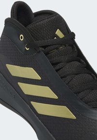 Scarpa sportiva nera con upper in tessuto testurizzato, dettagli dorati, tre strisce dorate distintive e lacci neri. Design sagomato imbottito.