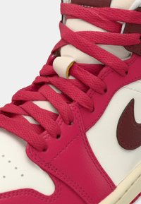 Gros plan d'une basket montante blanche et rouge avec des lacets rouges noués sur la languette rembourrée et un swoosh Nike rouge foncé sur le côté.