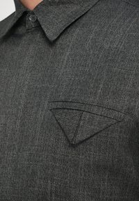 Siva denim srajca z značilnostmi pointed žepa, ovratnikom na gumb in subtilno teksturirano tkanino. Zaslon skrbno prikazuje šive in barvo.