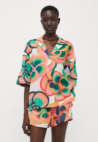 Fargerik kortermet skjorte og matchende shorts-sett, med et dristig blomsterdesign i grønt, rosa, oransje og marineblått på en lys bakgrunn.