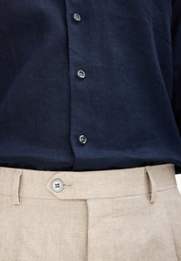 Camicia button-up in lino blu navy con sei bottoni. Pantaloni beige con chiusura a bottone e pieghe frontali. Tessuto liscio e vestibilità su misura.