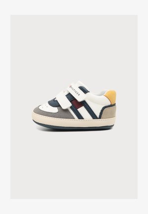 Baskets blanches pour enfant avec des accents bleu marine, gris, rouge et jaune, dotées de deux sangles velcro et d'une semelle en caoutchouc sur un fond uni.
