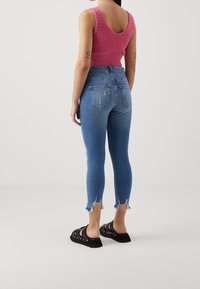 Růžový pletený tílko s výstřihem do V, doplněný o potrhané modré džíny s třepícím se lemem a zadními kapsami, dokončené černými sandály.