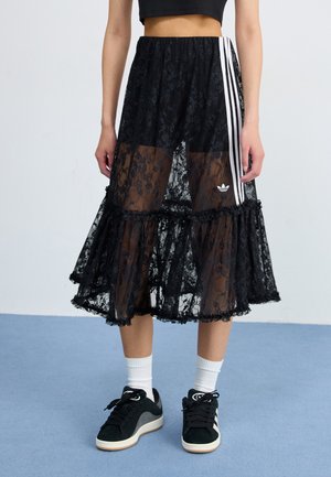 Black lace skirt with layered ruffles, sheer fabric, and white striped accents. Features an Adidas logo on the side, worn with black sneakers.