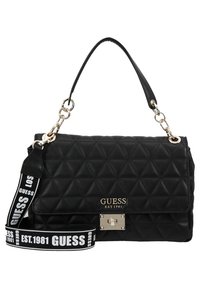 Sac à main matelassé noir Guess avec fermoir doré, poignée supérieure et bandoulière détachable avec logo blanc Guess et texte "EST. 1981".