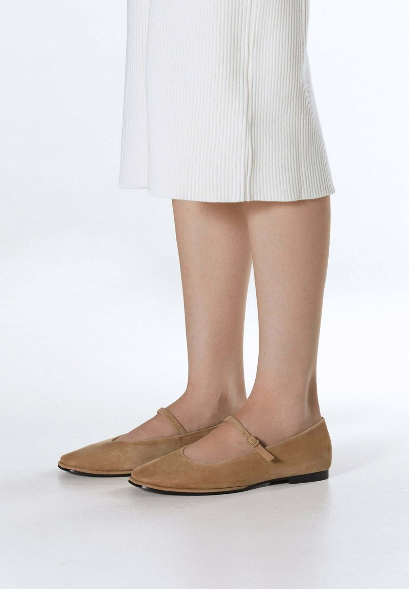 Beżowe zamszowe baleriny z ostrym noskiem, paskiem Mary Jane, niskim obcasem i delikatnym wycięciem po bokach. Gładka faktura z matowym wykończeniem.