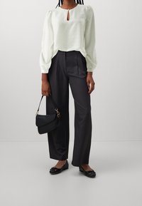 Camicia bianca con righe strutturate e scollatura a chiave, abbinata a pantaloni larghi grigi scuri. Borsa nera e scarpe basse con fiocchi.