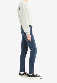 Felpa grigia, jeans blu e sneakers nere. I jeans sono a vestibilità slim con una texture liscia, e le sneakers hanno lacci bianchi e suole in gomma.