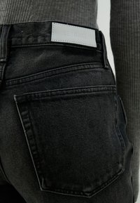 Jeans in denim nero con vita alta, tasche posteriori e un'etichetta in pelle bianca con la scritta "RE/DONE" in vita. Tessuto texturizzato.