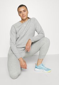 Conjunto de sudadera y pantalones de chándal grises, confeccionado en una tela suave, con cuello redondo y puños acanalados. Zapatillas deportivas azul claro con acentos amarillos.