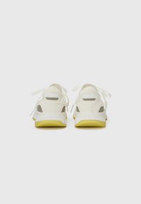 Baskets blanches avec une finition texturée, dotées d'accents gris et de semelles jaunes. Les lacets sont noués et il y a un contrefort de talon rembourré.