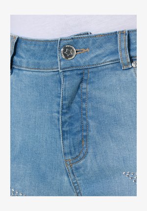 Shorts in denim azzurro chiaro con un bottone a scatto argentato e cuciture marroni. Borchie decorativi argentati abbelliscono la parte anteriore inferiore.