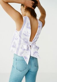 Hvid rygfri top med lavendelblomster mønstre og bindedetalje, sammen med lyseblå denim jeans. Glat stof og afslappet pasform.