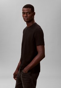 Zwart katoenen T-shirt met een ronde hals en korte mouwen, gecombineerd met grijze spijkerbroek. Eenvoudig, minimalistisch ontwerp zonder opvallende logo's.