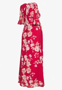 Robe maxi florale rouge avec des manches courtes évasées, dotée d'un dos en forme de clé et d'un mélange de fleurs roses et crème sur un tissu léger.