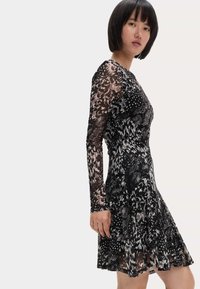 Abito a righe in bianco e nero con maniche lunghe, corpino aderente e gonna svasata; realizzato in un tessuto leggero e testurizzato.