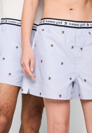Primo piano di due persone che indossano boxer a righe azzurro chiaro abbinate con piccoli motivi a stelle e fascia in vita con la scritta "tommy girl".
