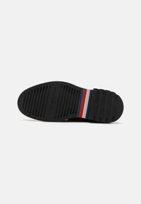 Talpa de pantof din cauciuc negru cu model texturat, prezentând un design cu dungi multicolore în roșu, alb și albastru. Numele mărcii este embossat.