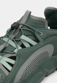 Αθλητικά παπούτσια με πλέγμα στο πάνω μέρος σε πράσινους τόνους, διαθέτουν υφασμάτινη σόλα από καουτσούκ με υφή, ελαστικό σύστημα κορδονιών και επενδεδυμένο κολάρο για άνεση.