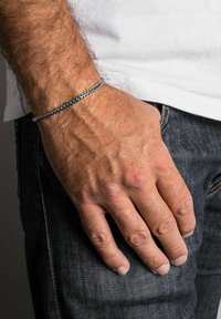 Patsaspael, millel on sile disain ja sujuv tekstuur, on randmel. Käsi toetub tumedale teksariidele.