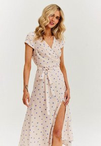 Jasnoróżowa sukienka o kroju w kształcie owinięcia, z niebieskimi wzorami muszelek, krótkimi rękawami i związanym w pasie krojem, z wysokim rozcięciem z jednej strony. Gładka tekstura materiału.