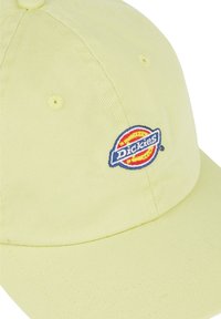 Boné de algodon amarelo com o logo bordado "Dickies" em vermelho e azul. Apresenta seis buracos de ventilação e uma aba curva.