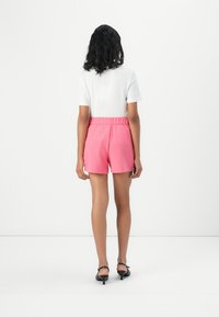 Shorts roses avec une taille élastique, associés à un haut blanc à manches courtes. Le modèle se tient de dos, mettant en valeur un design simple et moderne.