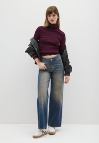 Dolcevita bordeaux a coste, jeans a gamba larga blu slavato a vita alta, giacca bomber nera e sneaker bianche con accenti blu navy.