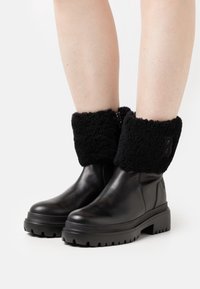 Czarne skórzane buty z grubą podeszwą, z czarnym futrzanym mankietem. Zamek błyskawiczny i fakturowane detale na podeszwie.