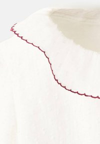 Biela tkanina so zubatým výstrihom a červeným prešívaním. Textúra vyzerá textúrovaná a na niektorých miestach mierne priehľadná.