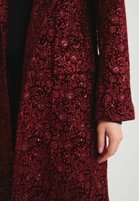 Manteau en velours bourgogne avec broderies florales élaborées et accents de sequins, à la coupe cintrée et aux manches longues.