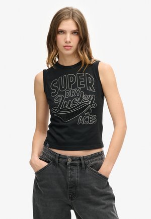 Black sleeveless crop top with white graphic text "SUPER DRY LUCKY ACES" and accent design. Worn with high-waisted dark gray jeans.