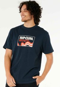 Camiseta de algodón azul marino con un gráfico rectangular audaz en blanco y naranja que presenta "RIP CURL" y un diseño de olas. Mangas cortas, cuello redondo.