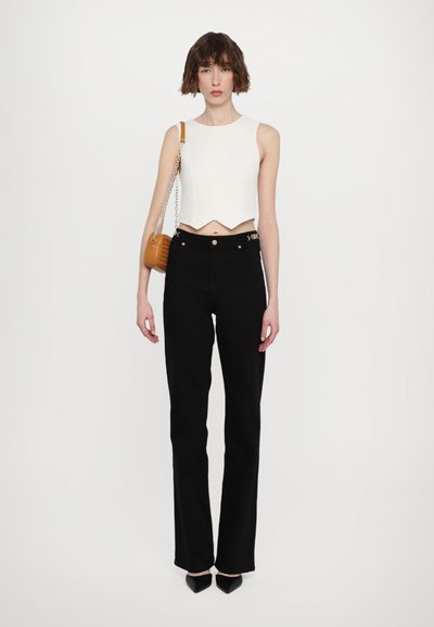 White cropped top with a wavy hem, paired with high-waisted black jeans, and an orange woven handbag. Black pointed-toe heels.