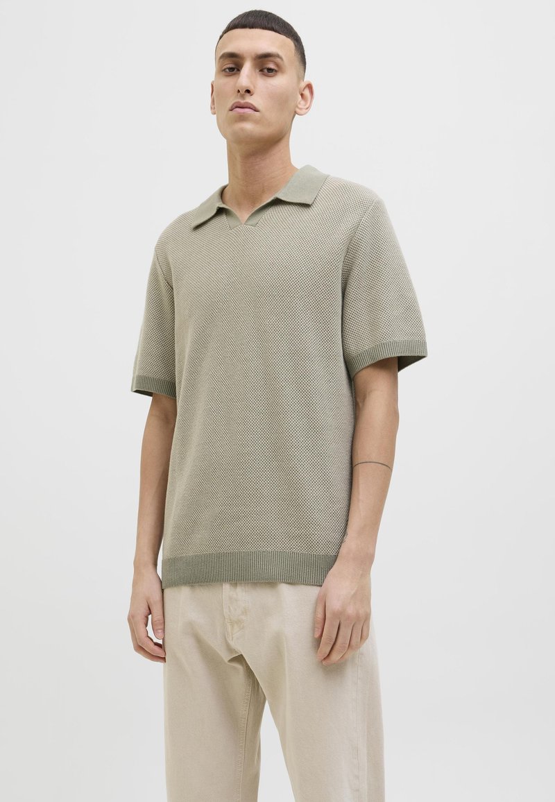 Lys grønn strikket polo skjorte med v-hals, korte ermer og ribbestrikkede mansjetter. Brukes sammen med beige bukser, som viser en teksturert stoff.