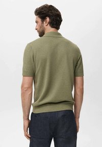 Polo à manches courtes en vert olive, texture côtelée, avec un col et une coupe ajustée, associé à un pantalon sombre et ample.