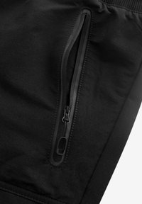 Sorte joggingbukser har en sidelomme med lynlås, elastisk talje og en glat stoftekstur. Designet er strømlinet med minimal dekoration.