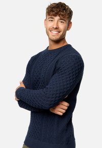 Granatowy sweter z dzianiny z teksturowanym wzorem zawierającym sploty w kształcie warkoczy oraz krzyżyków, z prążkowanym kołnierzem i mankietami, okrągłym wycięciem na szyję.