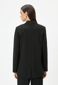 Blazer nero su misura con colletto appuntito, spacco singolo sul retro e tessuto morbido. Maniche lunghe e forma aderente.