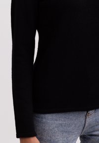 Schwarzer Pullover mit langen Ärmeln und weicher Textur. Der Saum ist gerade, und er wird mit hellblauen engen Jeans kombiniert.