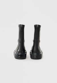 Bottines en cuir noir avec une semelle épaisse, dotées d'une fermeture éclair à l'arrière et d'un détail texturé sur la partie supérieure.