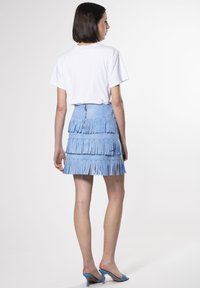 Lichtblauwe suède rok met een gelaagd franjes ontwerp, voorzien van zilveren studs en een rits aan de achterkant. Gepaard met een klassieke witte t-shirt en blauwe hakken.