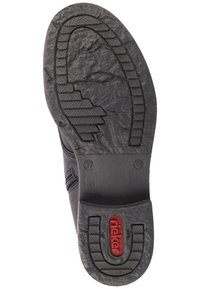 Suela de goma negra con agarre texturizado y patrón en zigzag. Presenta un logo rojo y marcaje de tamaño, área de punta lisa con ligera curvatura.