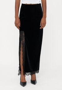 Fekete bársony maxi szoknya magas hasítékkal, bonyolult csipkeborítással. Siluettje karcsú, sima textúrával és elegáns dizájnnal rendelkezik.