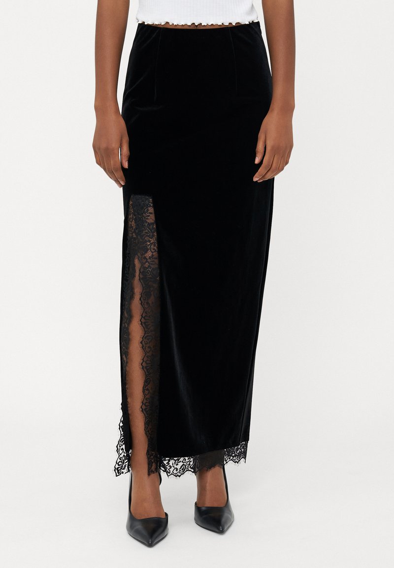 Fekete bársony maxi szoknya magas hasítékkal, bonyolult csipkeborítással. Siluettje karcsú, sima textúrával és elegáns dizájnnal rendelkezik.