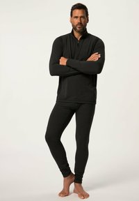Černý termo dlouhý rukáv s límcem na půl zip a černé legíny, obojí vyrobené z hladkého, pružného materiálu. Modelka stojí sebevědomě naboso.