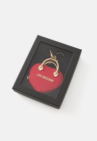 Raudona širdies formos raktų pakabuko piniginė, pagaminta iš tekstūruoto medžiagos, turi auksinės spalvos metalinę rankeną ir "LOVE MOSCHINO" logotipą. Pakuotė - juodas dėžutė.